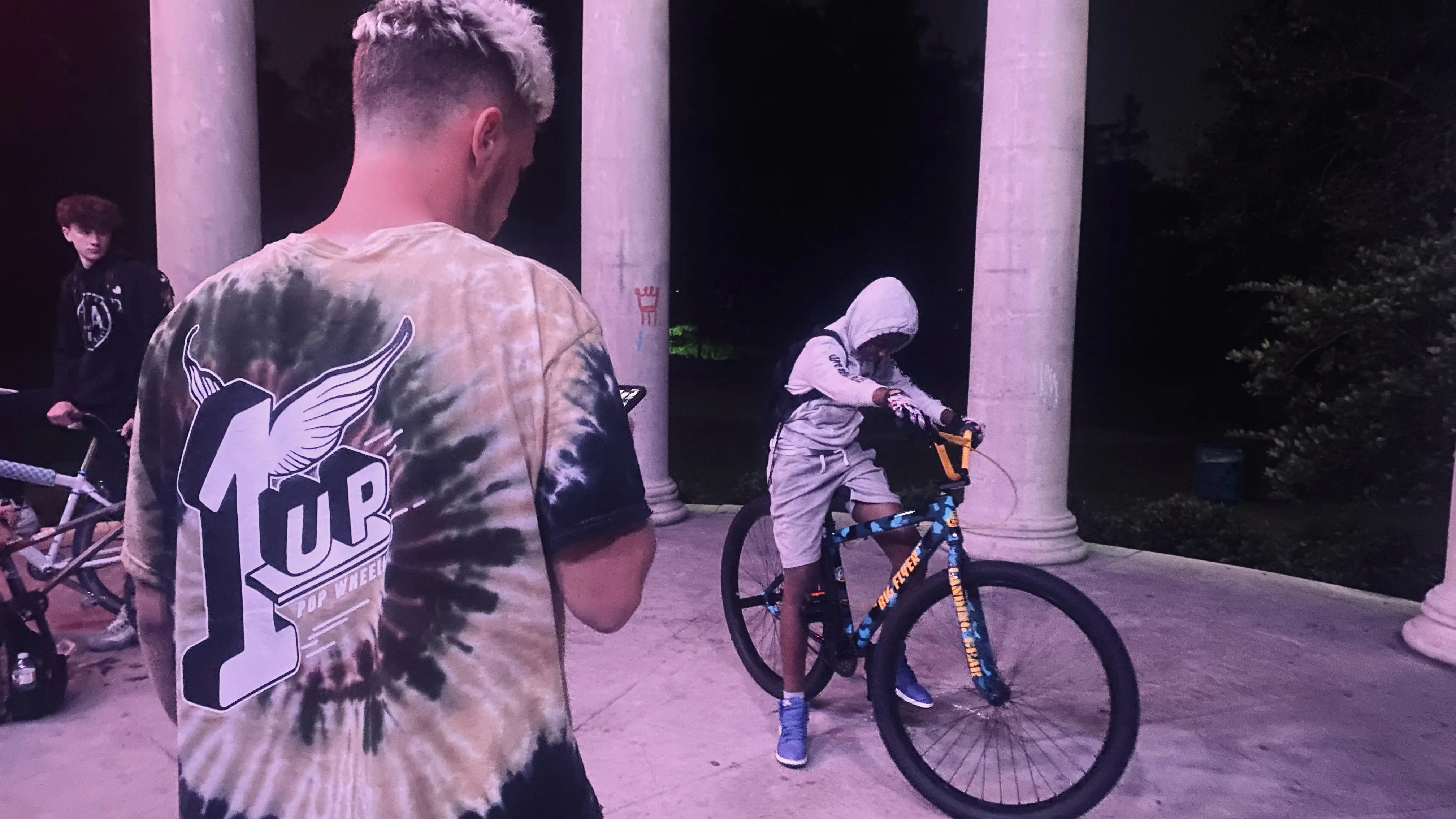 Crew posted up at night with a rider wearing a 1Up Bike Life shirt